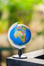 Vibrant miniature globe placed on a table, showcasing continents with blurred green background.
